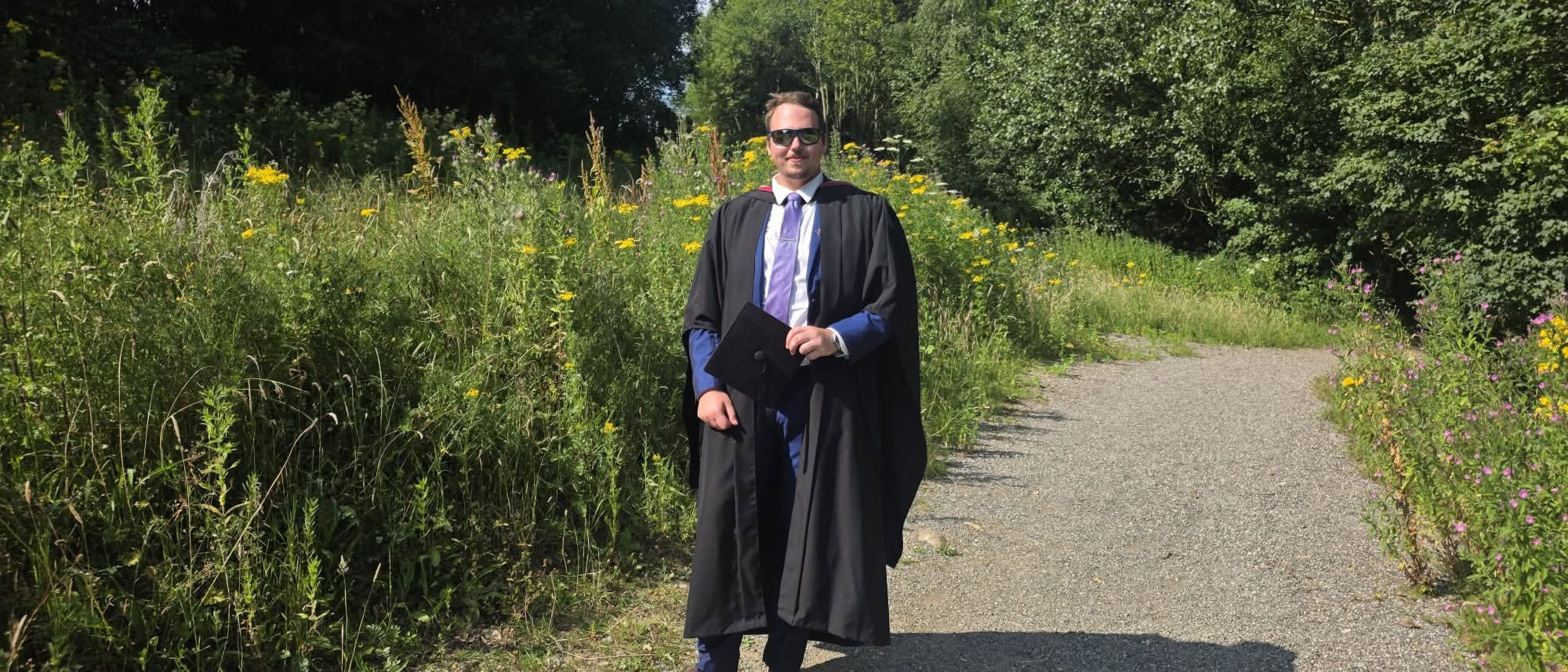 Dinas Stakeliunas in graduation robes on a wildflower-lined path